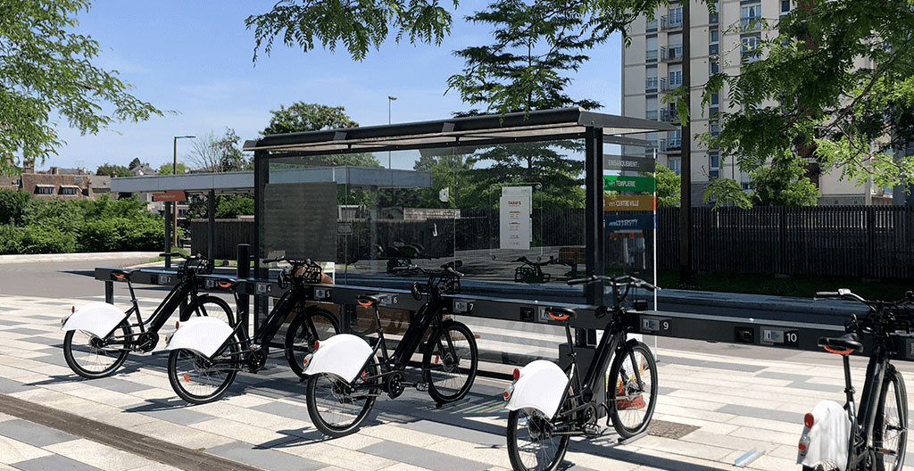 Station de vélopartage moderne avec vélos électriques arrimés, intégrée dans l'espace public français avec système de charge visible